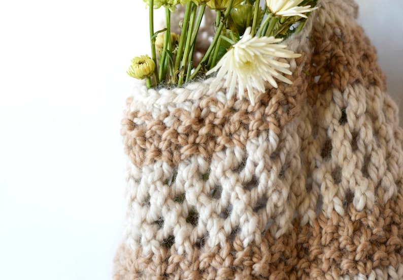 May include: A crocheted vase with a brown and white striped pattern. The vase is filled with dried flowers.