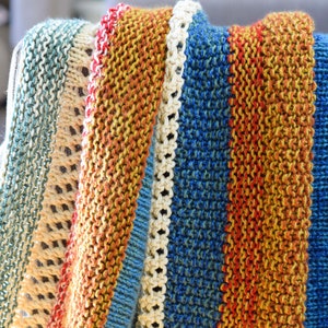 Pu&ograve; includere: Una coperta a righe di maglia in tonalit&agrave; di blu, arancione e crema. La coperta &egrave; piegata e drappeggiata su una sedia.