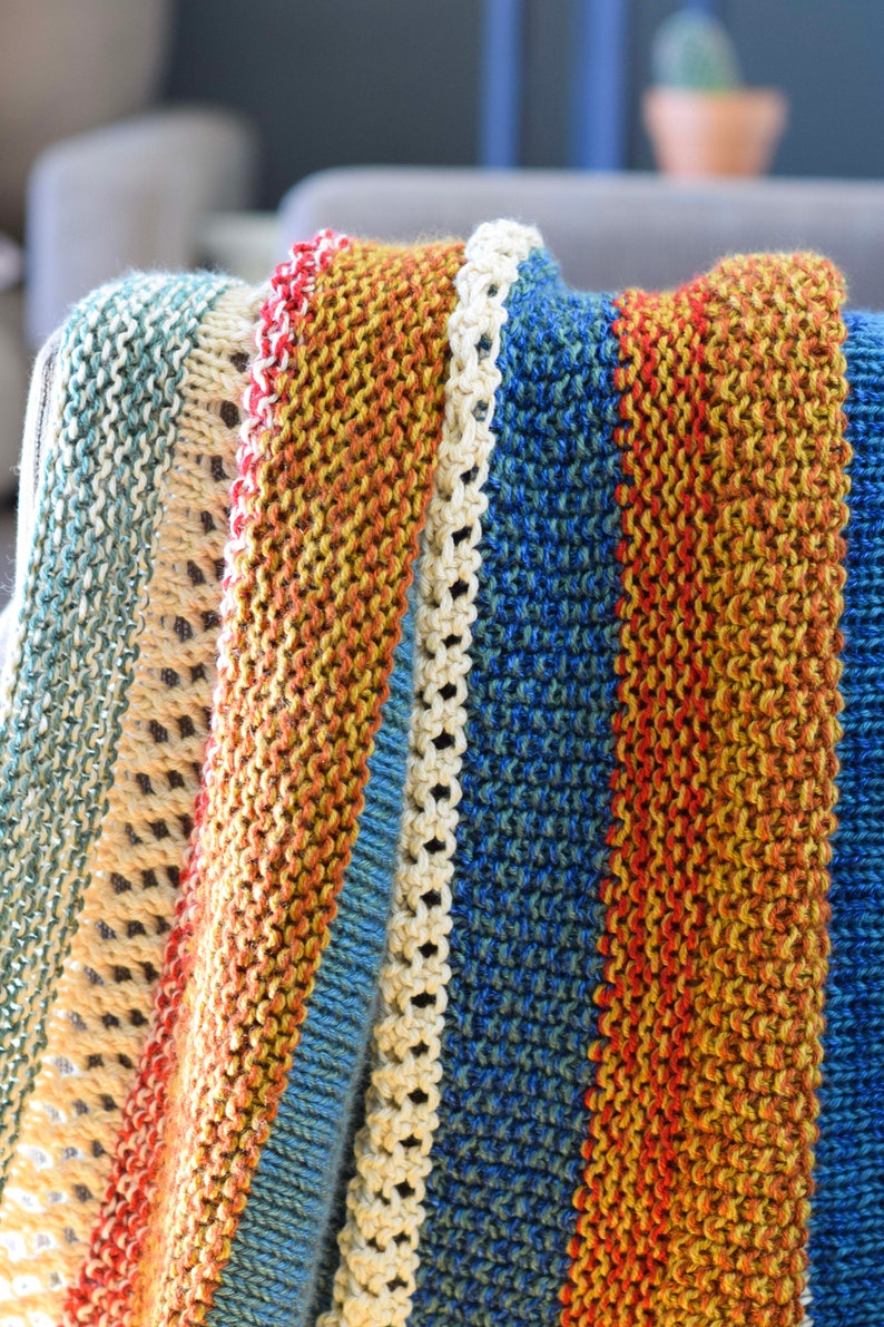 Pu&ograve; includere: Una coperta a righe di maglia in tonalit&agrave; di blu, arancione e crema. La coperta &egrave; piegata e drappeggiata su una sedia.