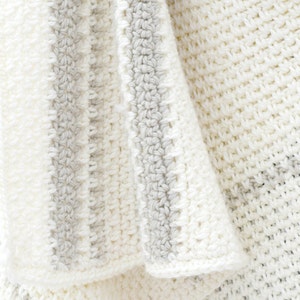 May include: A white crocheted blanket with gray stripes. The blanket is folded and draped over a surface.