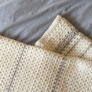 May include: A white and beige striped crocheted throw blanket with a soft, textured pattern.