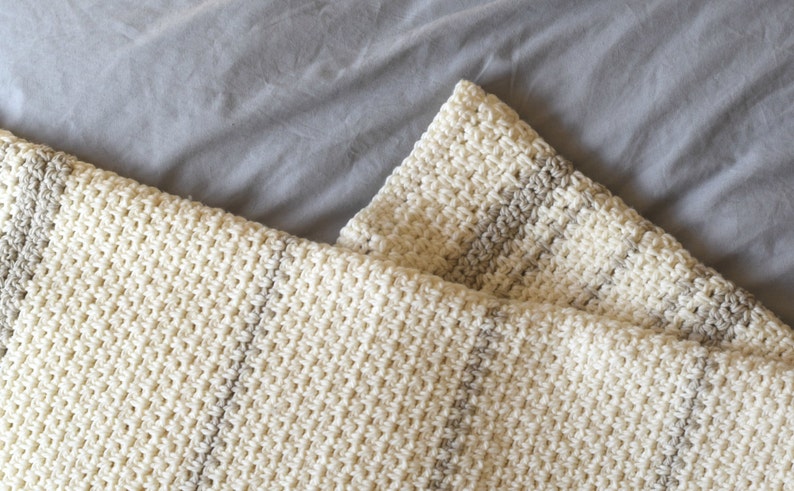 May include: A white and beige striped crocheted throw blanket with a soft, textured pattern.