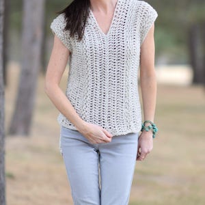 Puede incluir: Un top de crochet con cuello en V y mangas cortas. El top es de color beige claro y tiene un corte holgado y fluido.