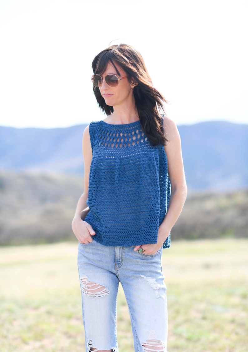 Pu&ograve; includere: Una donna indossa un top blu senza maniche all'uncinetto con un collo di pizzo e jeans di denim consumati.