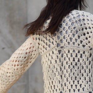 May include: A white crocheted cardigan with a lacy pattern. The cardigan has long sleeves and a loose fit.