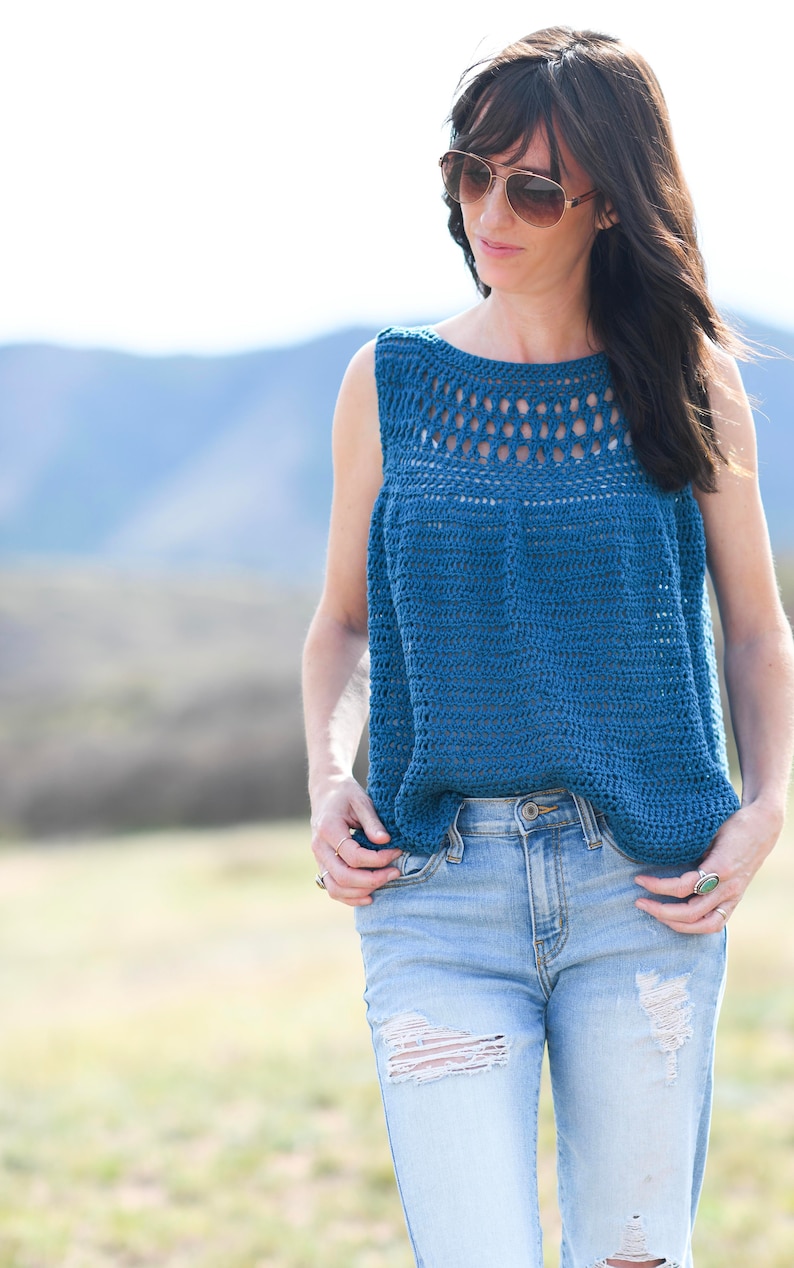 Pu&ograve; includere: Un top in crochet blu con scollo a pizzo e senza maniche. Il top &egrave; indossato con jeans blu chiaro.