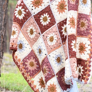 May include: A crocheted throw blanket with a patchwork design featuring various shades of brown, pink, and white. The blanket is made up of square motifs with a flower design in the center.