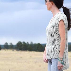Puede incluir: Un top de crochet sin mangas de color beige claro. El top tiene cuello en V y un corte holgado. La modelo lleva el top con un pantal&oacute;n gris claro.