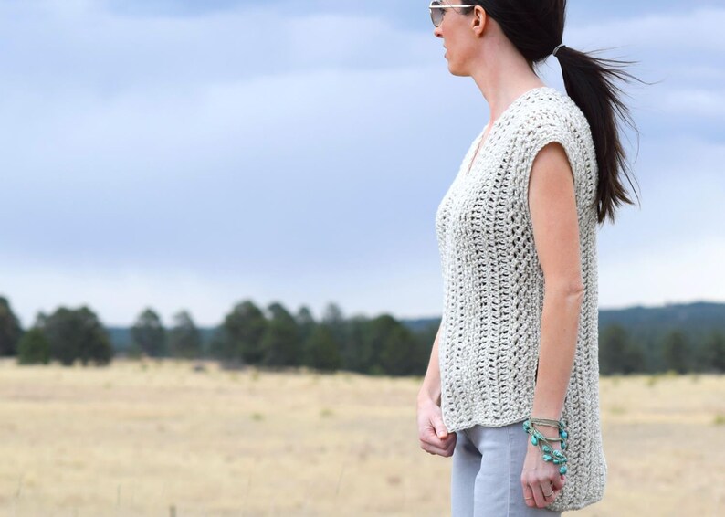 Puede incluir: Un top de crochet sin mangas de color beige claro. El top tiene cuello en V y un corte holgado. La modelo lleva el top con un pantal&oacute;n gris claro.