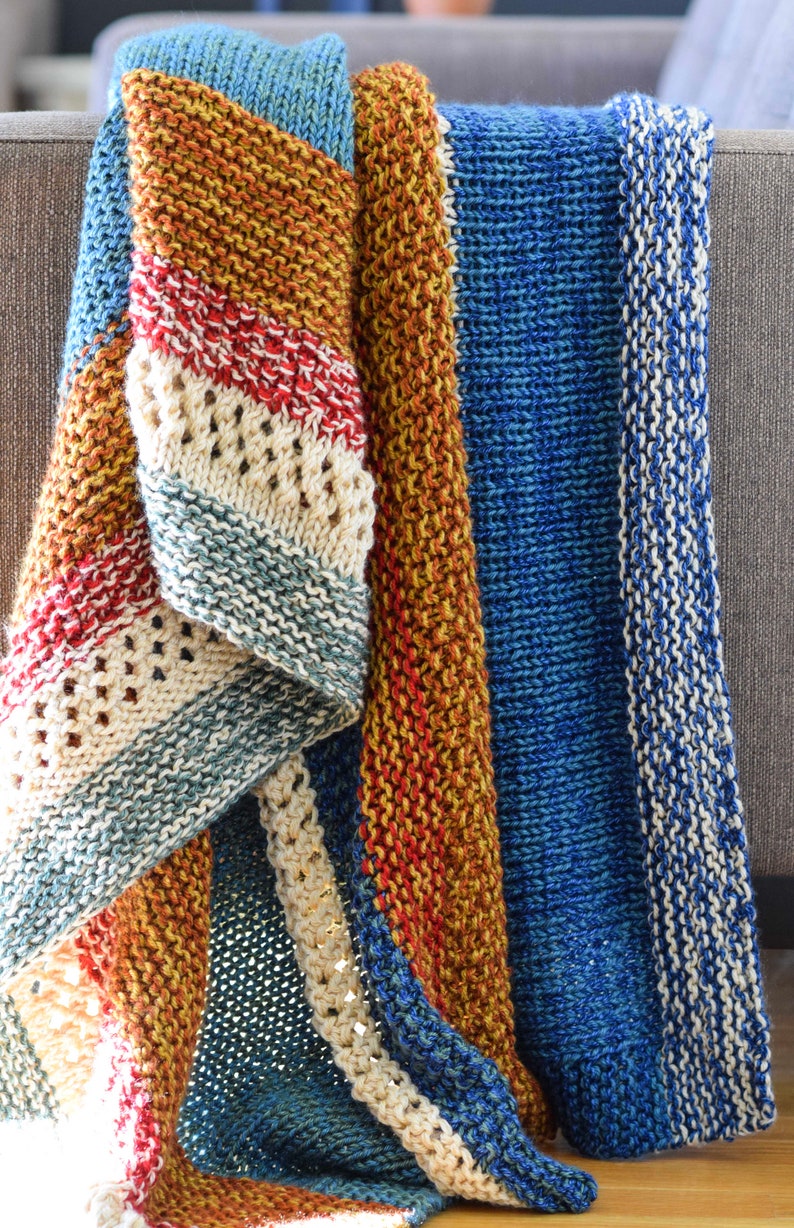 Pu&ograve; includere: Una coperta di lana a maglia multicolore con strisce blu, beige, rosse e arancioni. La coperta &egrave; piegata e drappeggiata su un divano.