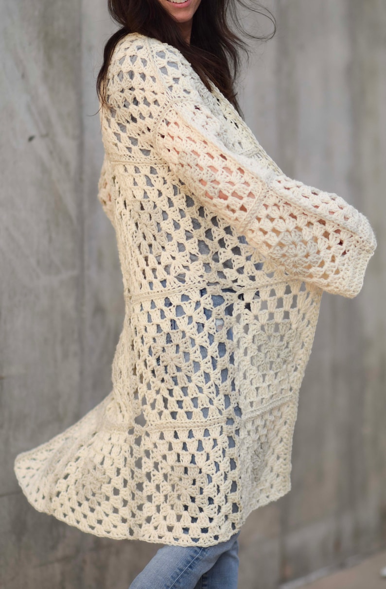 May include: A white crochet cardigan with a square pattern. The cardigan has long sleeves and a loose fit.
