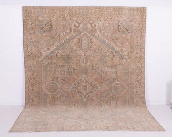 May include: A large, rectangular area rug with an intricate geometric pattern. The rug features a central diamond design in shades of brown, beige, and muted red, with accents of light blue. The overall design is symmetrical, with a border of repeating shapes.