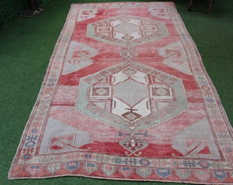 Puede incluir: Una alfombra turca vintage con un patrón geométrico rojo, verde y blanco. La alfombra tiene un aspecto descolorido y desgastado y está hecha de lana.