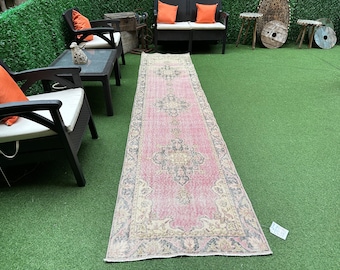 May include: A pink and cream vintage runner rug with a floral pattern. The rug is laid out on a green artificial grass surface.