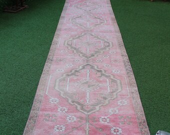 May include: A rectangular, vintage-style rug with a pink central field and intricate geometric patterns in shades of beige and brown. The rug features a border with floral motifs and measures approximately 3 feet wide.