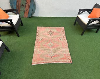 Può includere: Un tappeto rosa e beige con un motivo a rombi al centro. Il tappeto è su una superficie di erba artificiale verde.