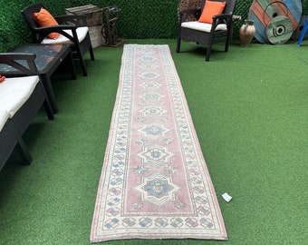 May include: A pink and white patterned runner rug with a geometric design. The rug is laid out on a green artificial grass surface.