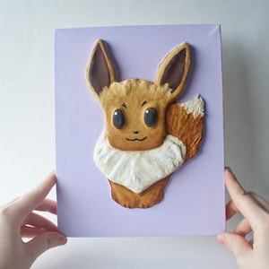 May include: A hand-painted, three-dimensional Eevee Pokemon sculpture on a purple canvas. The sculpture is made of brown, white, and orange clay.