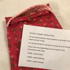 May include: A red and white floral print potato cooker bag with a pink and white checkered lining. The bag has a printed instruction sheet that reads "POTATO COOKER INSTRUCTION:" and details on how to use the bag.