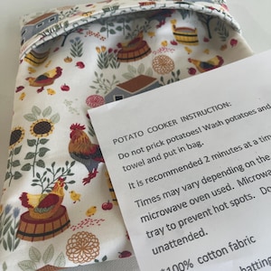 Puede incluir: Una bolsa de tela para cocinar patatas con fondo crema y un estampado colorido de granja con gallos, gallinas, pollitos, girasoles y casitas. Una tarjeta de instrucciones blanca está colocada encima detallando el uso en microondas.