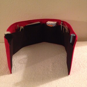 May include: Red felt organizer with multiple compartments for a purse or handbag. The organizer has a black felt lining and includes a small white brush, a small blue tube, and a small white box with blue and white text.