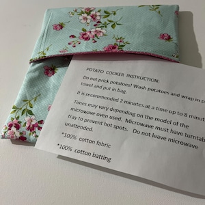 May include: A light blue microwave potato cooker with a floral pattern in pink and white. The instructions for use are included on a white paper. The cooker is made of 100% cotton fabric and batting.
