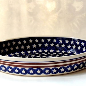 May include: An oval ceramic baking dish featuring a deep blue interior patterned with small white stars. The exterior displays a horizontal brown stripe above a band of blue circles, each containing a white star, set against a cream background.