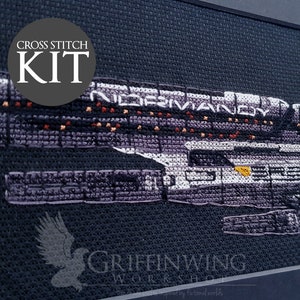 Puede incluir: Kit de punto de cruz que representa la nave espacial Normandy de la serie de videojuegos Mass Effect. La imagen muestra la nave en tonos morados, negros y blancos, con el texto "NORMANDY" y "CROSS STITCH KIT".