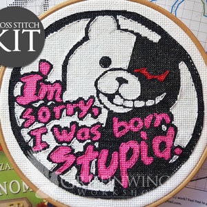 Puede incluir: Kit de punto de cruz con un diseño de personaje en blanco y negro y el texto rosa "I'm sorry I was born stupid". El diseño está en un bastidor de bordado de madera. También se ven las palabras "Cross Stitch Kit".