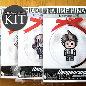 Op de afbeelding: Kruissteekpakketten met gepixelde karakterontwerpen. Elke set bevat een ronde borduurring met een voltooid kruissteekbeeld, een rood lint en de tekst "Danganronpa 2 Goodbye Despair Cross-Stitch Kit". De sets zijn verpakt in doorzichtig plastic.