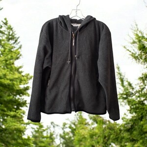 Könnte beinhalten: Ein dunkelgrauer Fleece-Hoodie mit Reißverschluss und Kapuze. Der Hoodie hat eine Reißverschlusstasche auf der linken Seite.