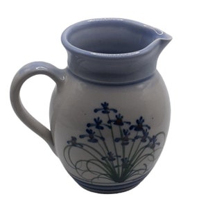 Könnte beinhalten: Ein kleiner, weißer Keramik-Krug mit einem blauen und grünen Blumendesign. Der Krug hat einen runden Körper und einen Henkel.