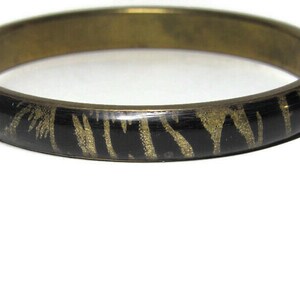 May include: A gold bangle bracelet with a black and gold zebra print design.