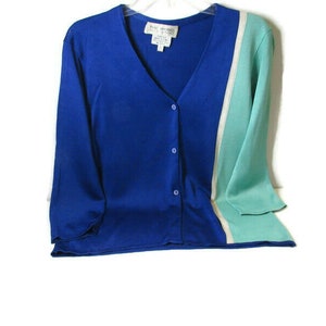 May include: A blue and green striped cardigan with a white stripe down the center. The cardigan has a v-neck and button closure.