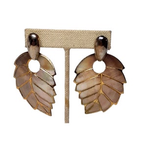 Può includere: Un paio di orecchini a forma di foglia dorati e iridescenti. Gli orecchini sono in metallo e hanno un design delicato e intricato.