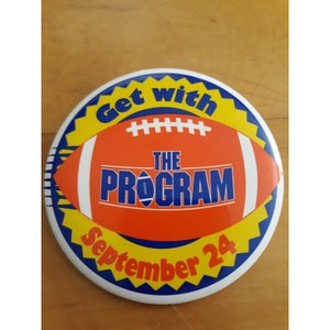 Könnte beinhalten: Ein runder Knopf mit einem gelben Sternburst-Design und einem blauen Rand. In der Mitte befindet sich ein rot-weißer Fußball mit dem Text "Get with The Program September 24".