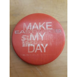 May include: Red round button with white text that reads "Make Eastwoood  My Day".
