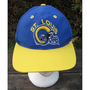 May include: A blue and yellow baseball cap featuring the St. Louis Rams logo. The cap has a blue crown with the team name and logo in yellow. The brim is yellow. The cap is likely made of a durable fabric.