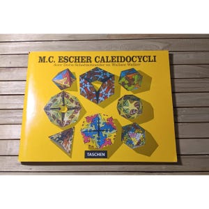 May include: A yellow book titled "M.C. Escher Kaleidocycli" with various colorful geometric shapes. The book cover features the TASCHEN logo. The shapes are in shades of blue, green, yellow, and red.