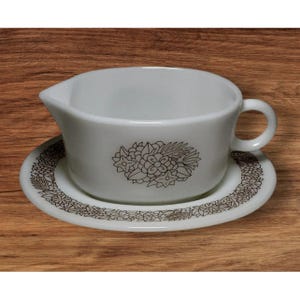 Puede incluir: Juego de salsera y platillo blancos con diseño floral marrón. La salsera tiene asa y pico vertedor. El platillo presenta un borde floral a juego. El juego es de cerámica, ideal para servir salsas.