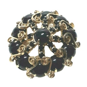 May include: A gold tone brooch with a circular design featuring black cabochon stones and gold filigree accents.