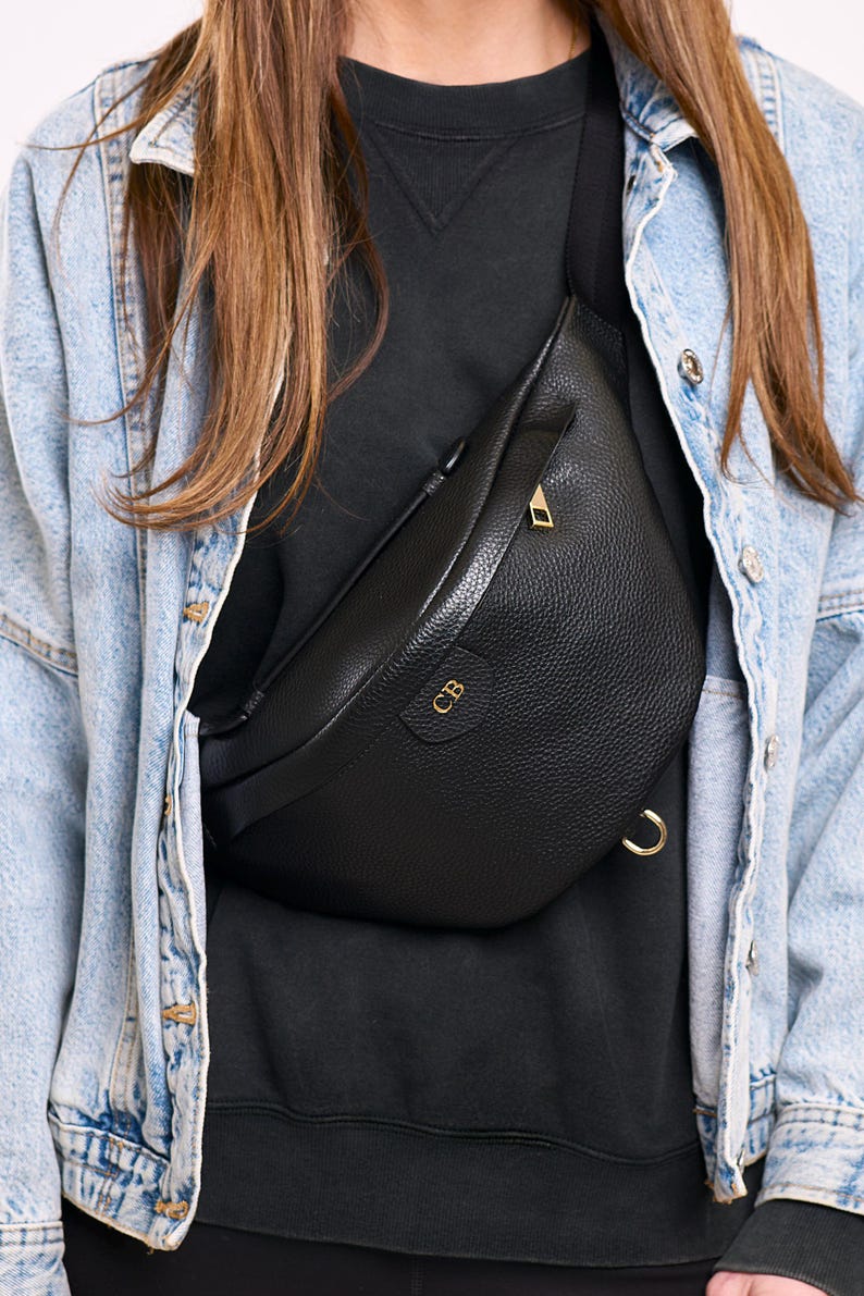 Peut inclure: Un sac banane en cuir noir grain&eacute; dot&eacute; d'une fermeture &eacute;clair dor&eacute;e et d'un anneau en D en m&eacute;tal dor&eacute; sur le c&ocirc;t&eacute;. L'avant du sac est emboss&eacute; avec les lettres dor&eacute;es CB. Le sac est port&eacute; en bandouli&egrave;re avec une sangle noire r&eacute;glable.