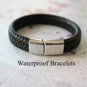 Op de afbeelding: Een zwarte leren armband met een zilveren sluiting. De armband is gevlochten en heeft een eenvoudig ontwerp. Waterdichte armbanden.