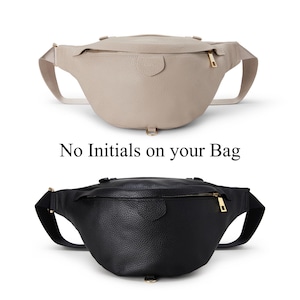 Peut inclure: Un sac banane beige et un sac banane noir, tous deux dot&eacute;s d'une surface textur&eacute;e, d'une fermeture &eacute;clair sup&eacute;rieure avec une tirette dor&eacute;e et d'une sangle r&eacute;glable. Le texte "No Initials on your Bag" est plac&eacute; entre les deux sacs superpos&eacute;s.