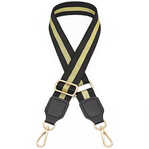 May include: A replacement bag strap featuring a black and gold woven pattern with a central gold stripe. The strap includes a gold metal adjustable slider and two black faux leather end tabs, each finished with a gold metal swivel lobster clasp.