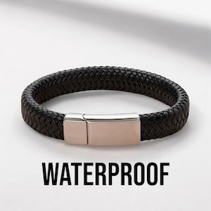 Peut inclure: Un bracelet en cuir tressé noir doté d'un fermoir en métal poli de couleur or rose. Le mot WATERPROOF est imprimé en lettres capitales noires sous le bracelet, qui est présenté sur un fond clair et uni.
