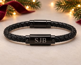 Puede incluir: Una pulsera de cuero trenzado negro con una pieza central rectangular de metal negro pulido grabada con las letras SJB. La pulsera incluye un mecanismo de cierre magnético de metal negro a juego para un cierre seguro.