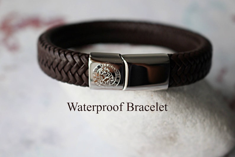 Op de afbeelding: Een bruin leren armband met een zilveren sluiting en een klein zilveren embleem. De armband is gelabeld "Waterdichte armband".