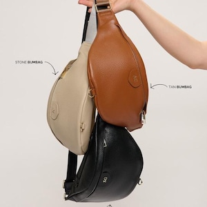 Peut inclure: Trois sacs banane en couleurs pierre, fauve et noir, chacun pr&eacute;sentant une finition textur&eacute;e, une fermeture &eacute;clair et une sangle r&eacute;glable. Les sacs sont &eacute;tiquet&eacute;s STONE BUMBAG, TAN BUMBAG et BLACK BUMBAG avec des fl&egrave;ches les d&eacute;signant.