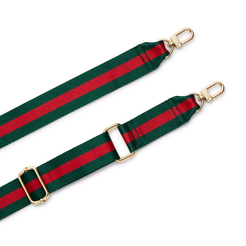 May include: A replacement bag strap featuring a woven green and red striped pattern. The strap includes gold-toned metal hardware, specifically two lobster claw clasps at the ends and two adjustable sliding buckles along the length of the fabric.